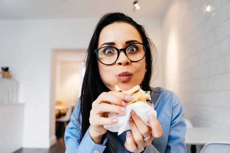 Mujer con gafas comiendo un sándwich sentada en la oficina